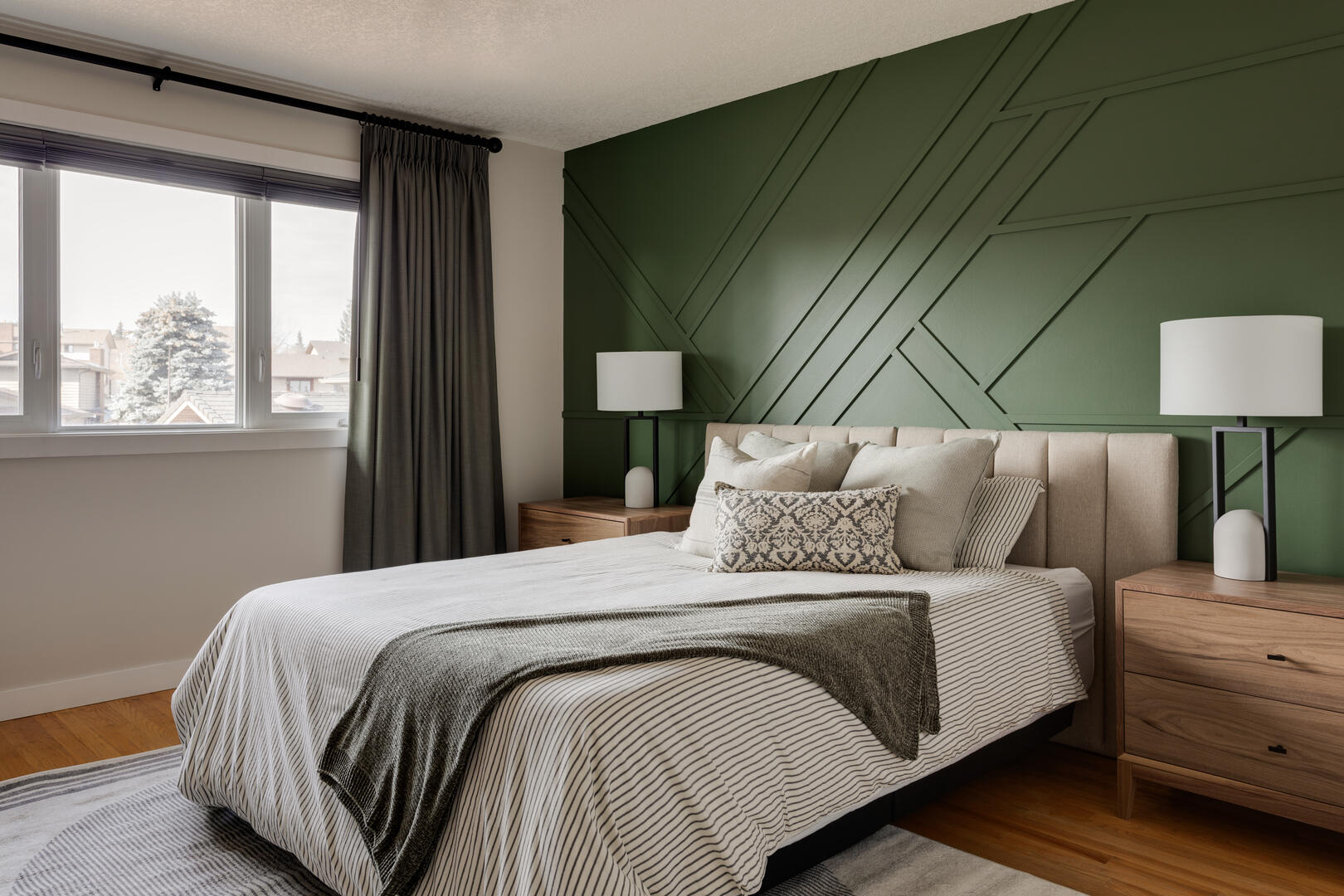 Bright primary bedroom with green accent wall, wood furniture and neutral decor